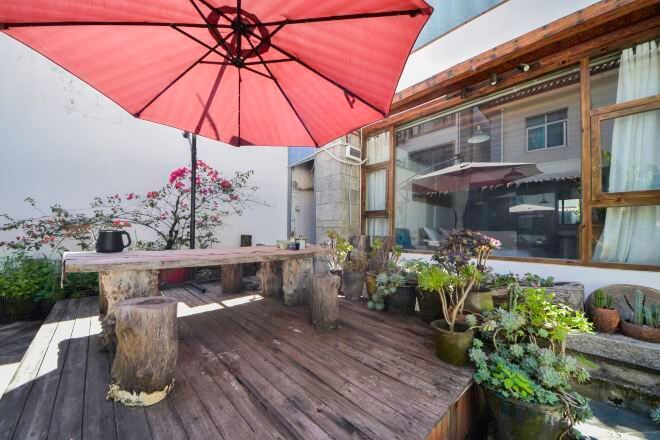 An outdoor patio with a wooden table, a red umbrella, and potted plants.