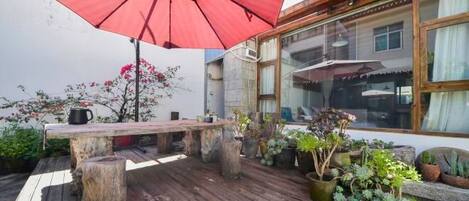An outdoor patio with a wooden table, a red umbrella, and potted plants.