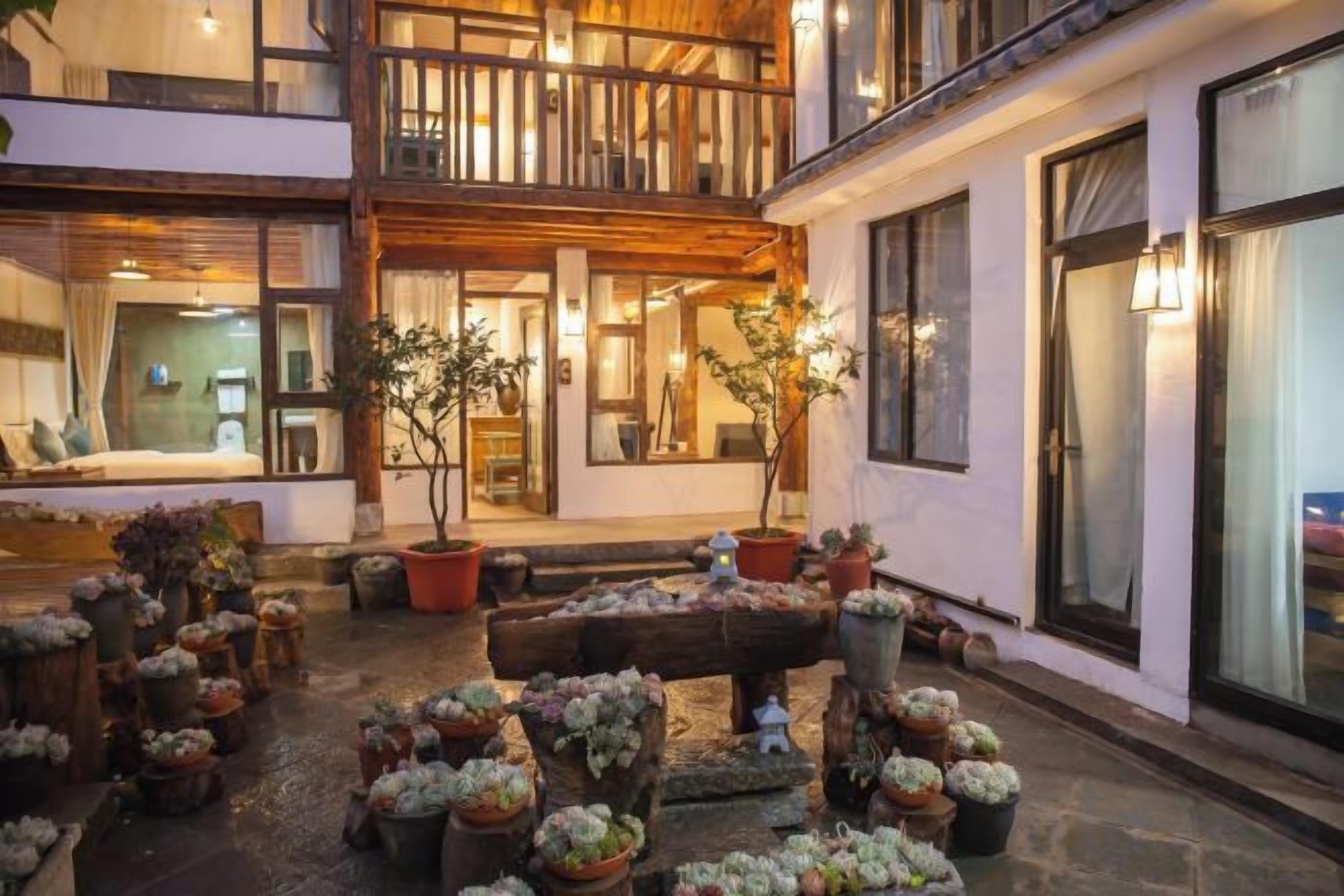 A courtyard with potted plants, a wooden bench, and a building with a balcony.