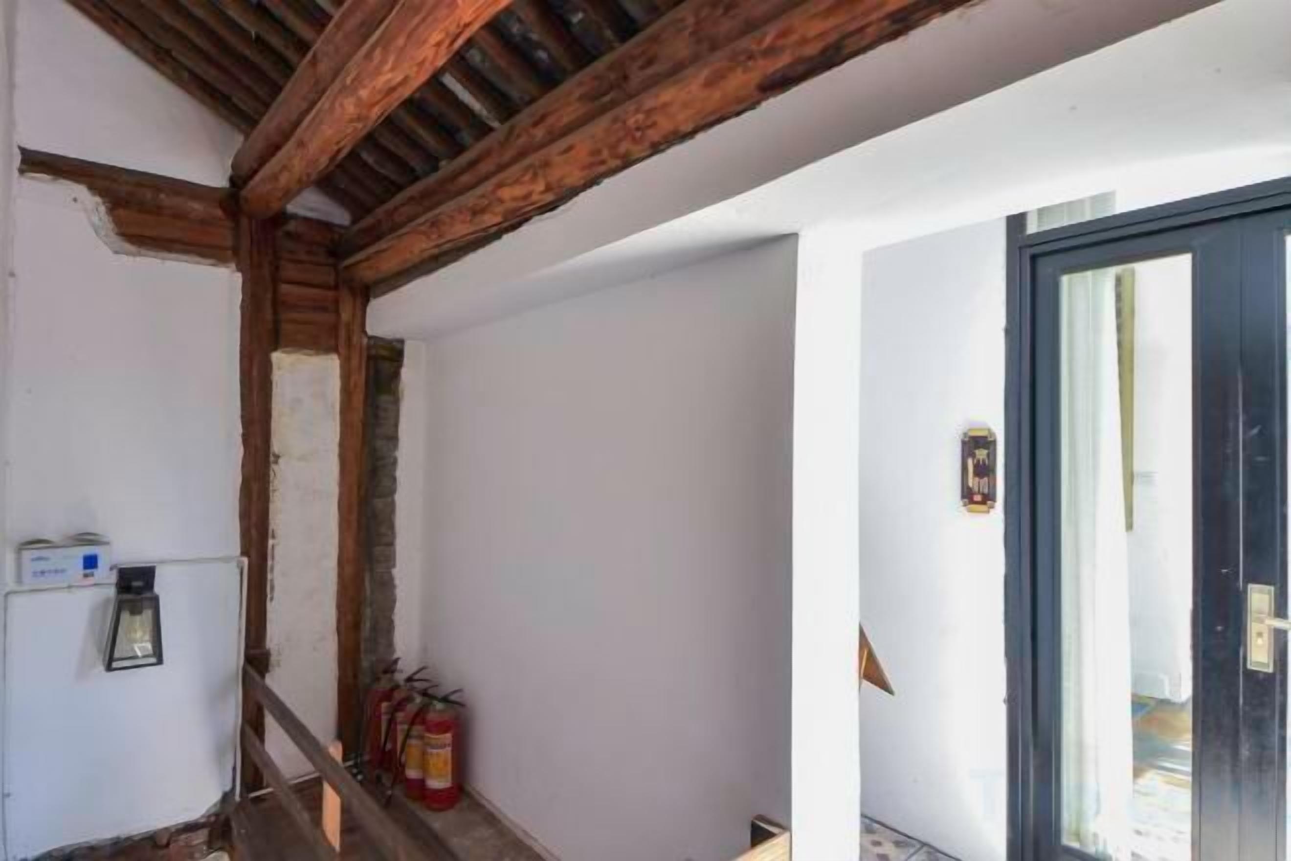 A room with exposed wooden beams, a door with a glass panel, and a fire extinguisher on the wall.