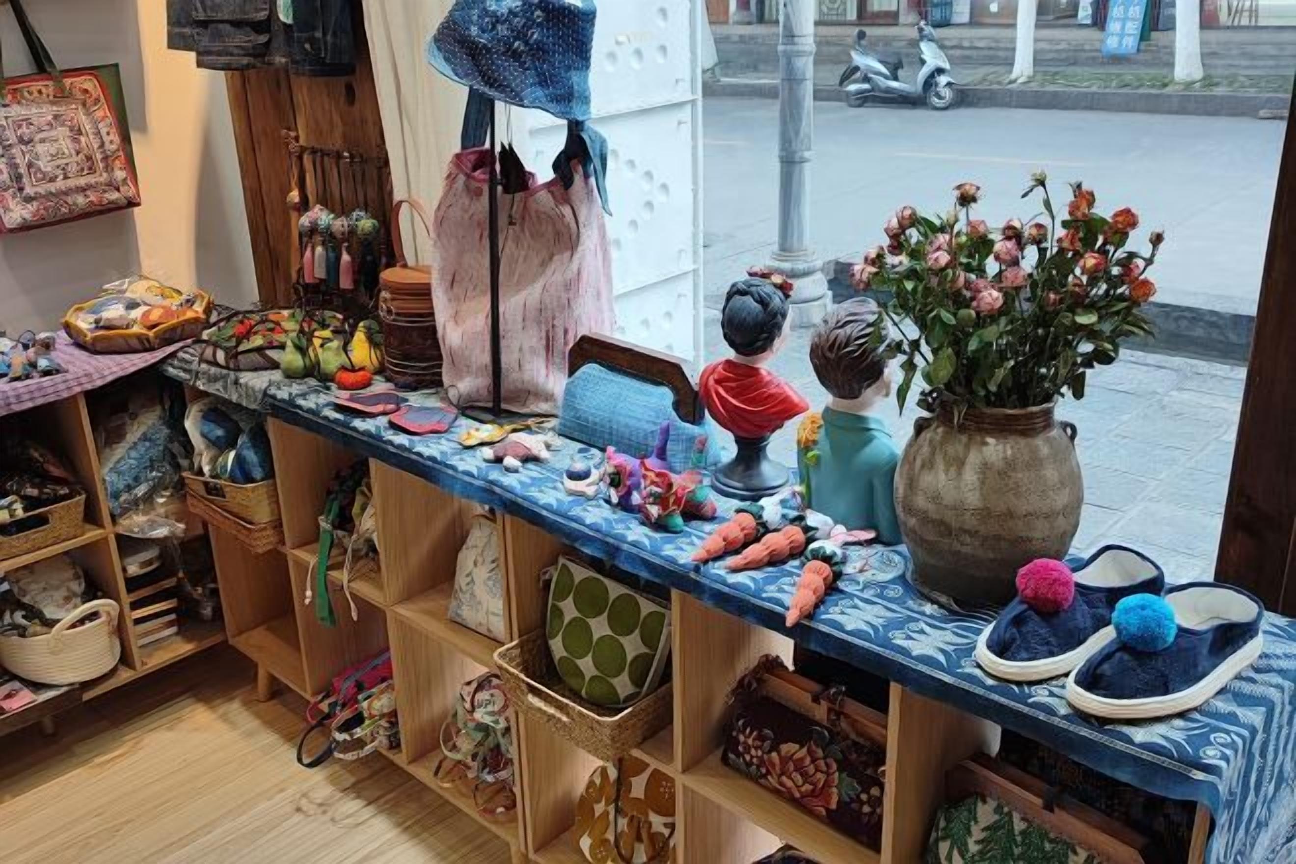 A room with a wooden floor, a window with a view of the street, and a table with various items including a vase with flowers.