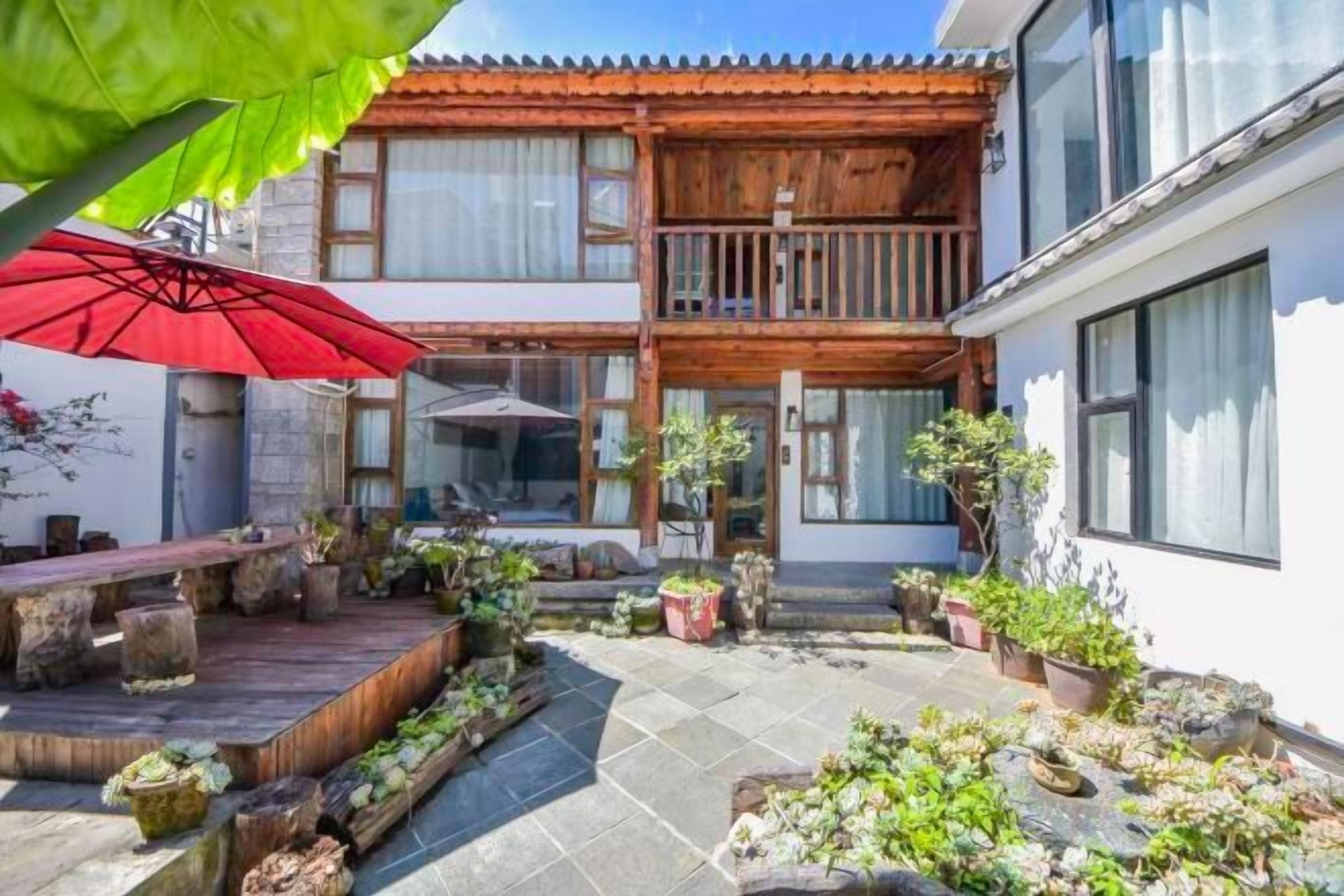 A courtyard with a wooden balcony, potted plants, and a red umbrella.