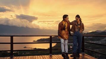 A couple standing on a wooden deck overlooking a body of water with mountains in the background.
