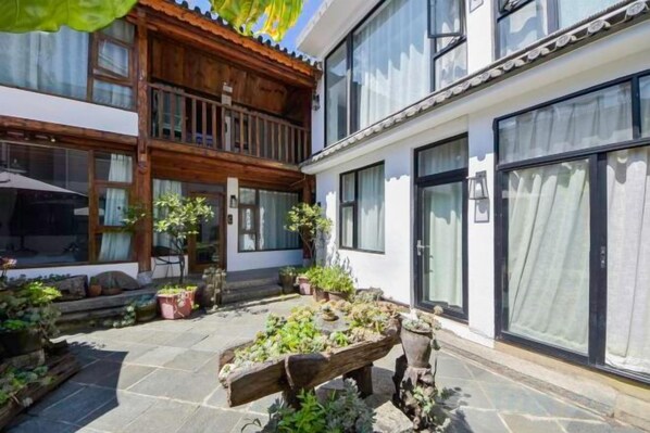 A courtyard with potted plants, a wooden bench, and a building with large windows.