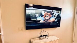 A television mounted on a wall, a white cabinet with decorative carvings, and a small house-shaped plant holder on the cabinet. - * Comfy Condo close to everything in Prattville * (Prattville)
