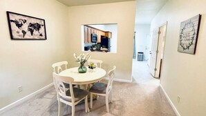 A dining area with a round table, white chairs, and a vase with flowers. There are two framed pictures on the walls, one of a world map and another with the word "LOVE". - * Comfy Condo close to everything in Prattville * (Prattville)