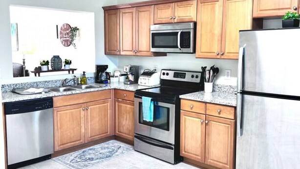 A modern kitchen with wooden cabinets, stainless steel appliances, and a blue patterned rug. - * Comfy Condo close to everything in Prattville * (Prattville)