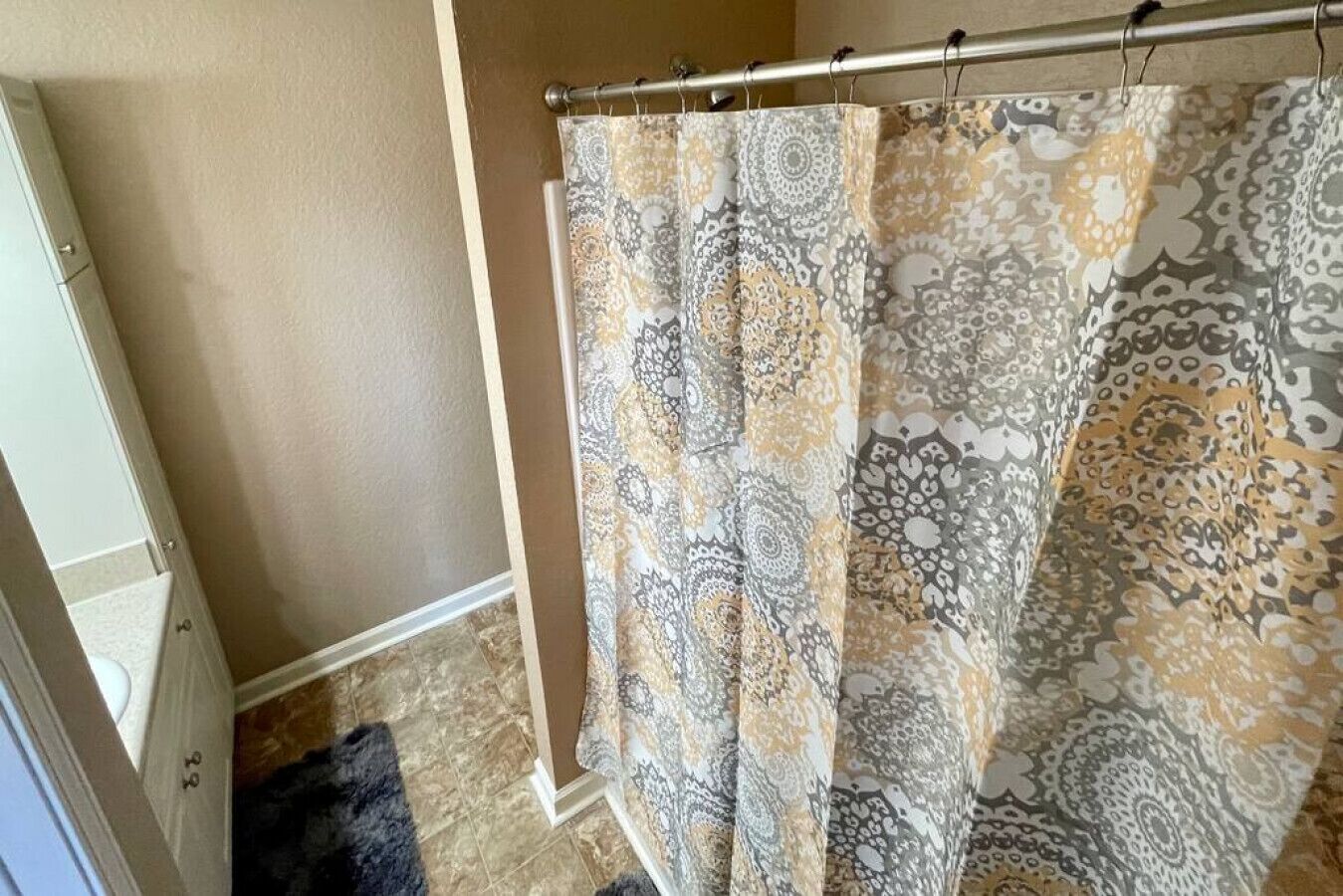A bathroom with a patterned shower curtain, a tiled floor, and a door with a number.