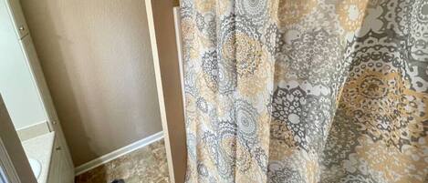 A bathroom with a patterned shower curtain, a tiled floor, and a door with a number.