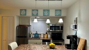 A modern kitchen with a granite countertop, stainless steel appliances, and pendant lighting. - Beautifully updated one bedroom one bath 4th-floor unit (Marco Island)