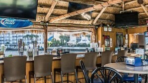 A bar area with wooden furniture, a thatched roof, and a view of the sea. - Beautifully updated one bedroom one bath 4th-floor unit (Marco Island)