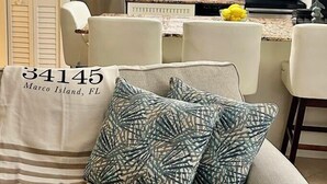 A living room with a sofa, a dining area with chairs and a table, and a kitchen with appliances and pendant lights. - Beautifully updated one bedroom one bath 4th-floor unit (Marco Island)