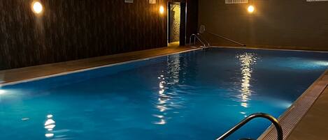 Una piscina interior con agua cristalina, una escalera metálica e iluminación empotrada.