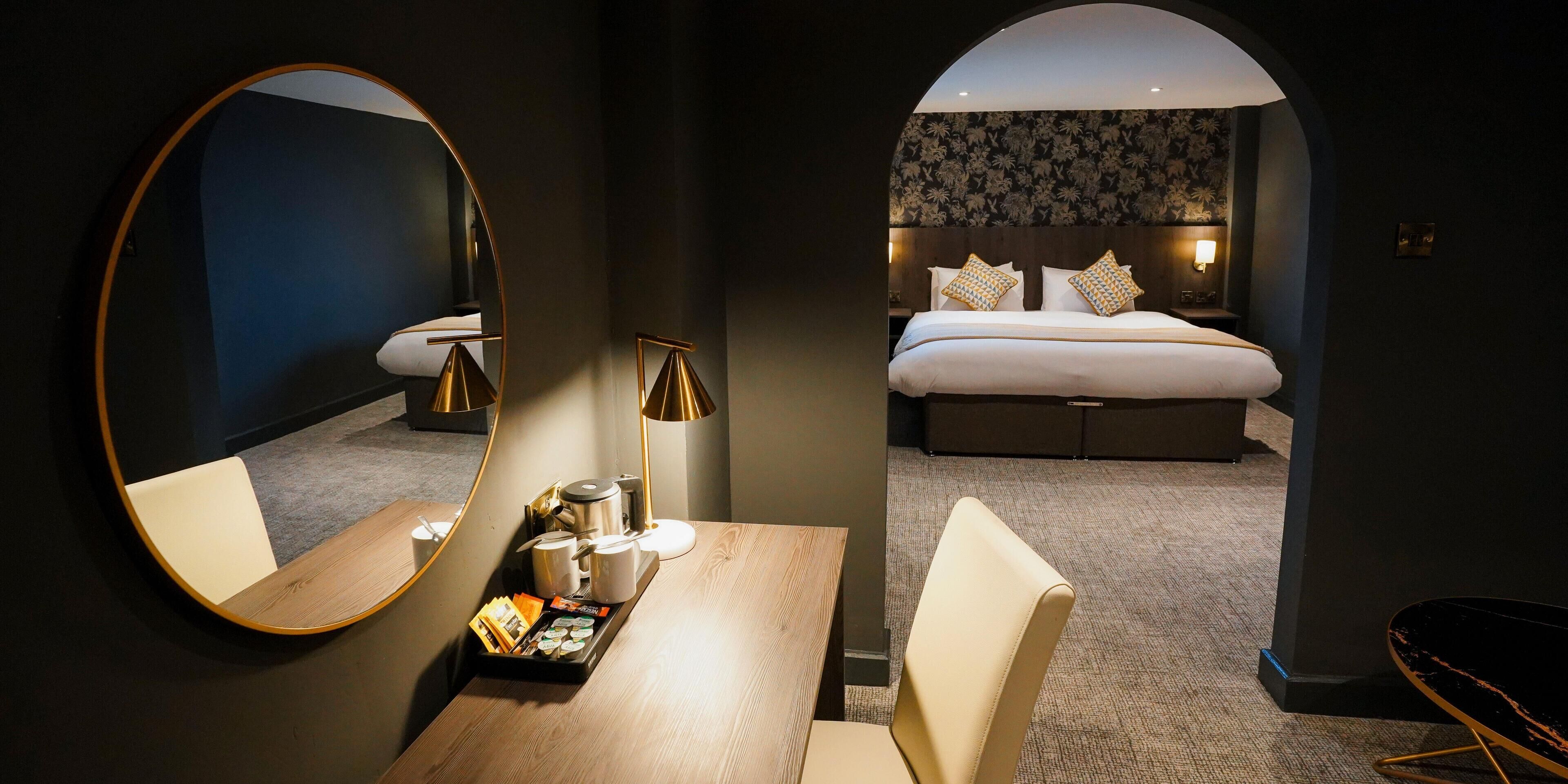 Habitación de hotel con cama, escritorio y bandeja de desayuno, espejo redondo y lámpara.