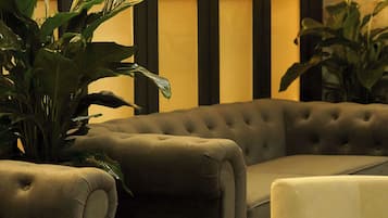 A room with a tufted sofa, a white armchair, and a large potted plant.