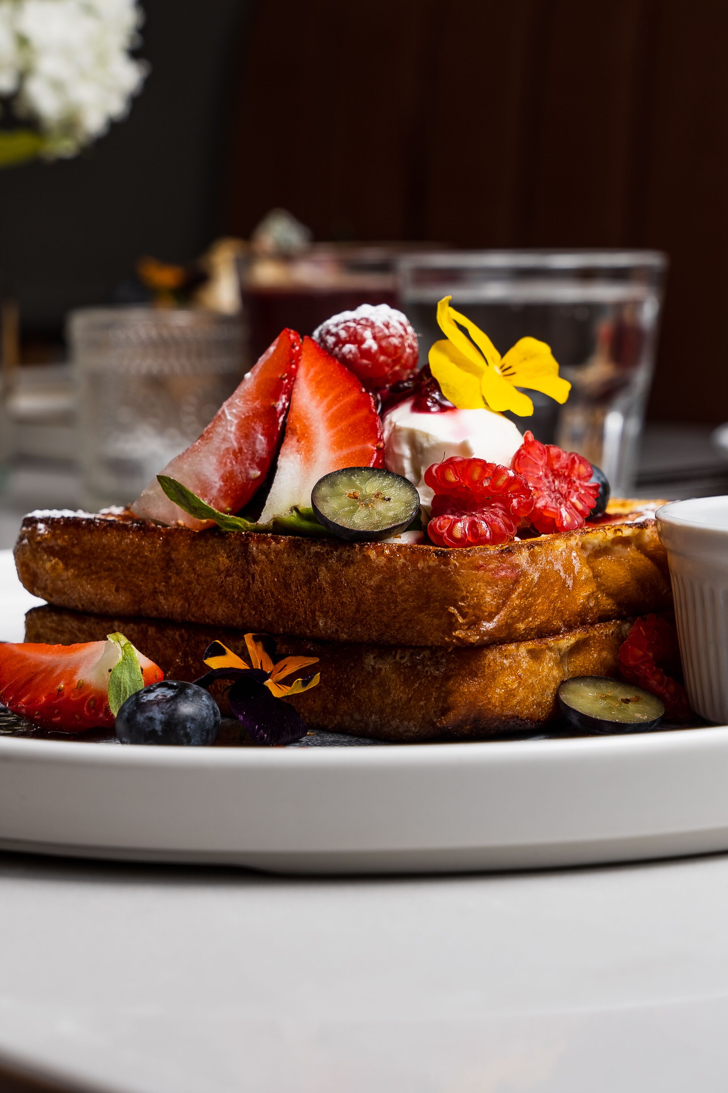 A plate of French toast with strawberries, raspberries, and a yellow flower garnish.