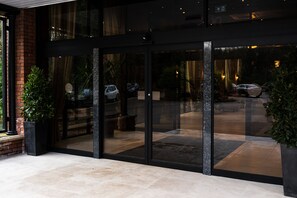A modern building entrance with glass doors, a brick wall, and potted plants. - Park Hall Hotel & Spa Lancashire, a member of Radisson Individuals (Chorley)