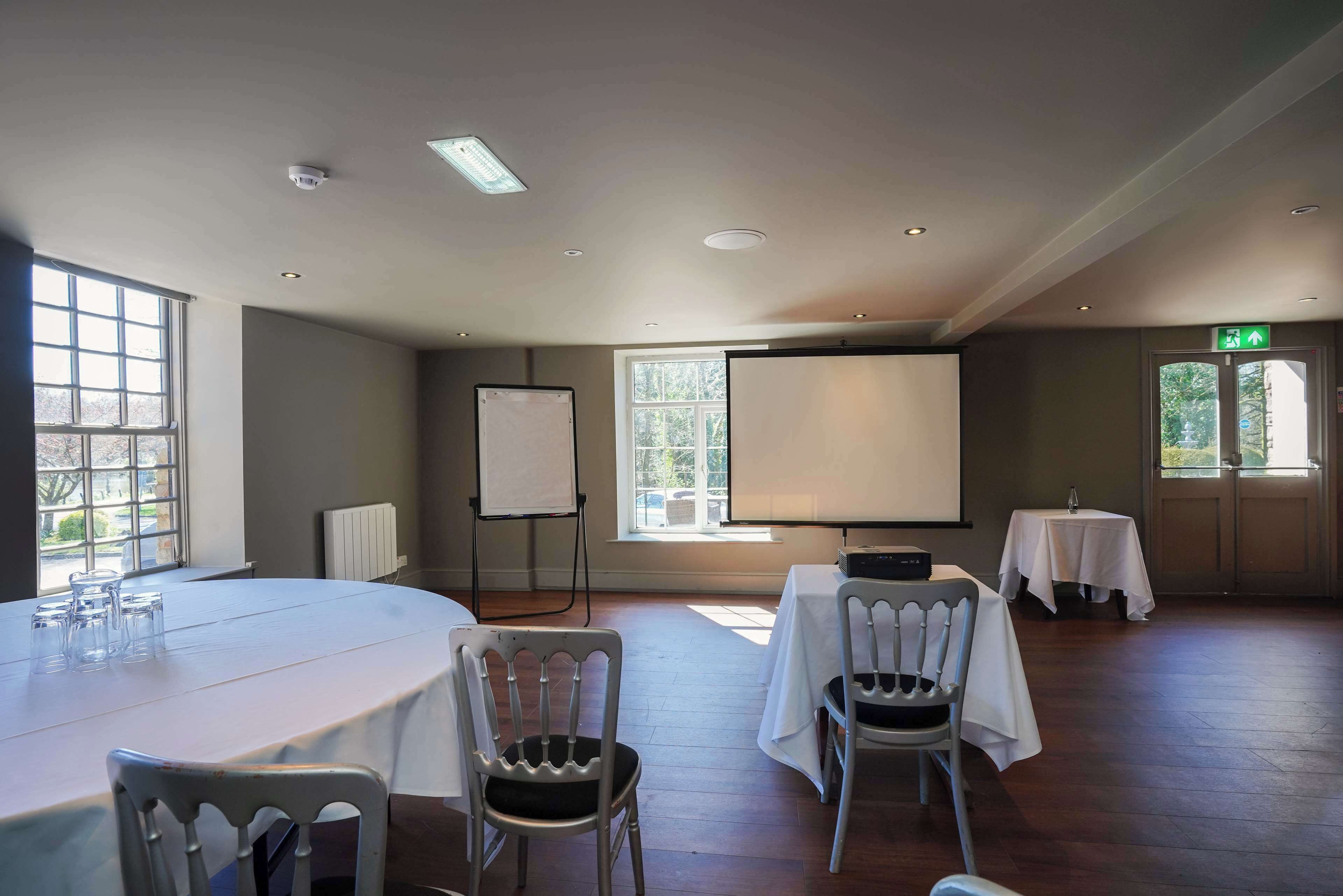 A conference room with a large oval table, two chairs, a projector, and a whiteboard.