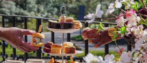 A three-tiered dessert stand with pastries and a drink on a wooden table outdoors.