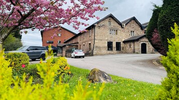 A stone building with a brick facade, two cars parked in front, and a well-maintained garden with various plants and flowers.