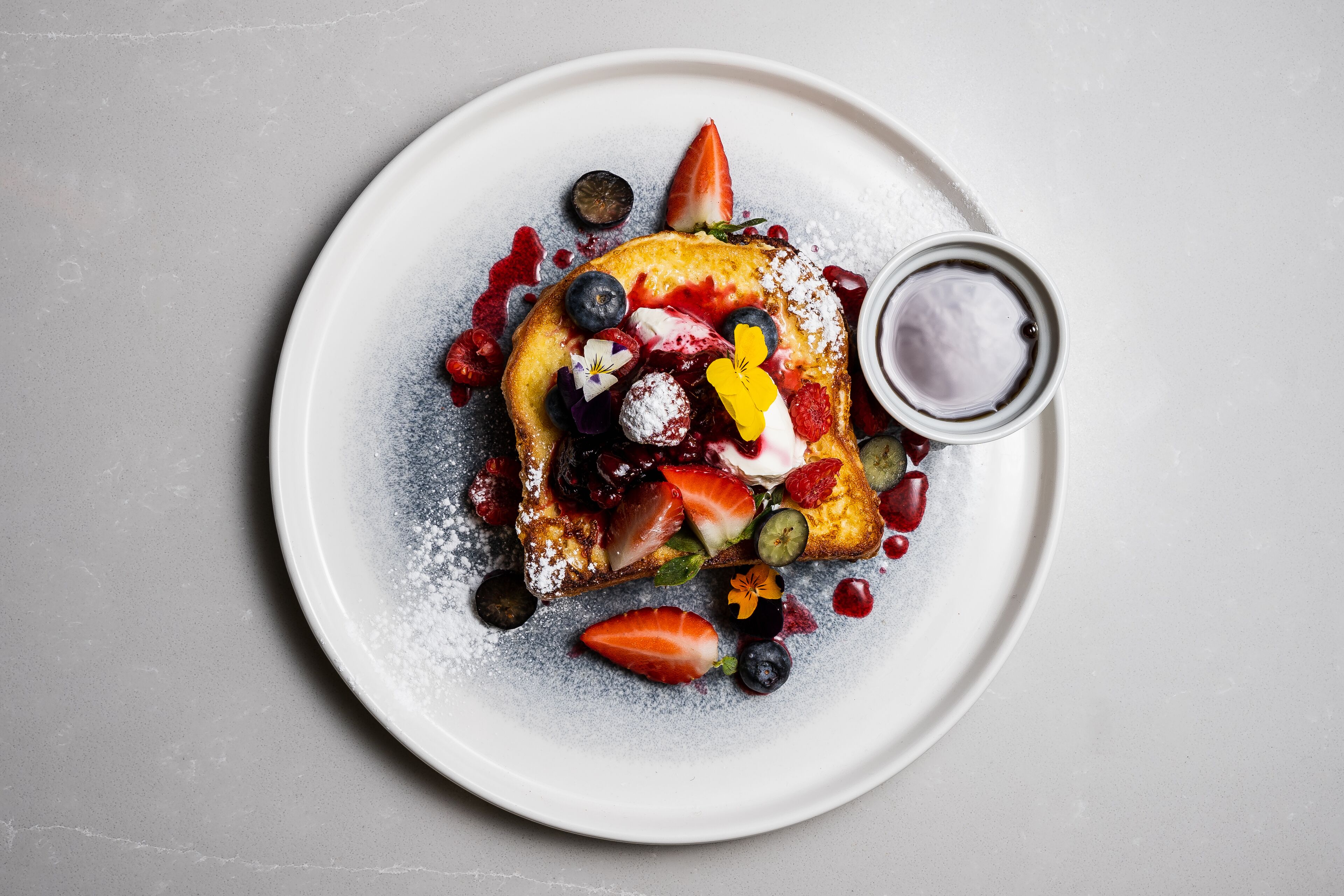 A plate with a dessert topped with strawberries, blueberries, and a dollop of cream, dusted with powdered sugar.