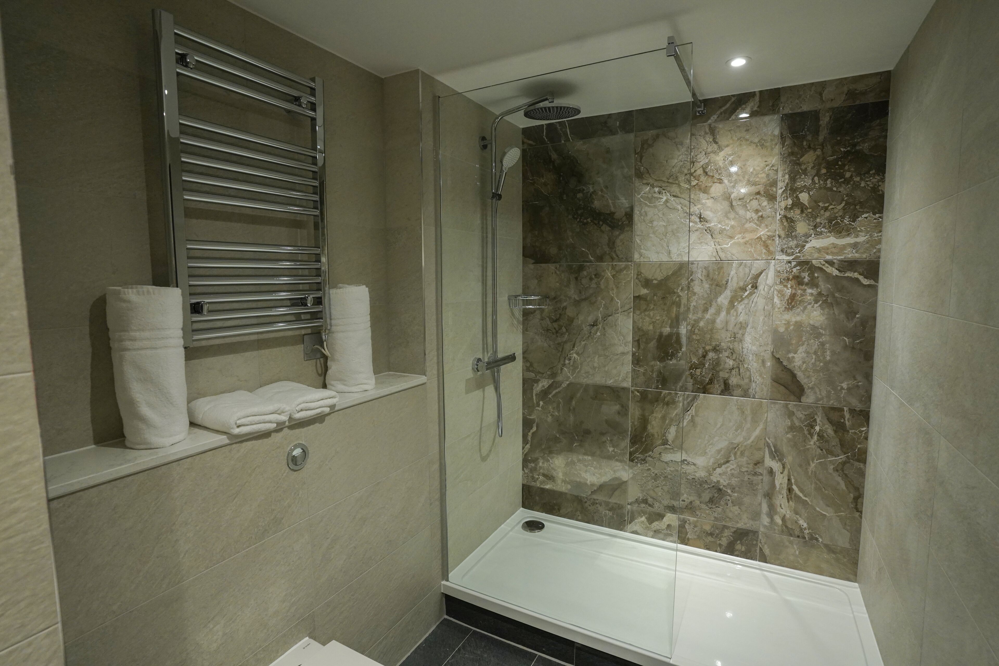 Une salle de bain moderne dotée d’une douche à parois de verre, de carreaux de marbre et d’un porte-serviettes intégré.