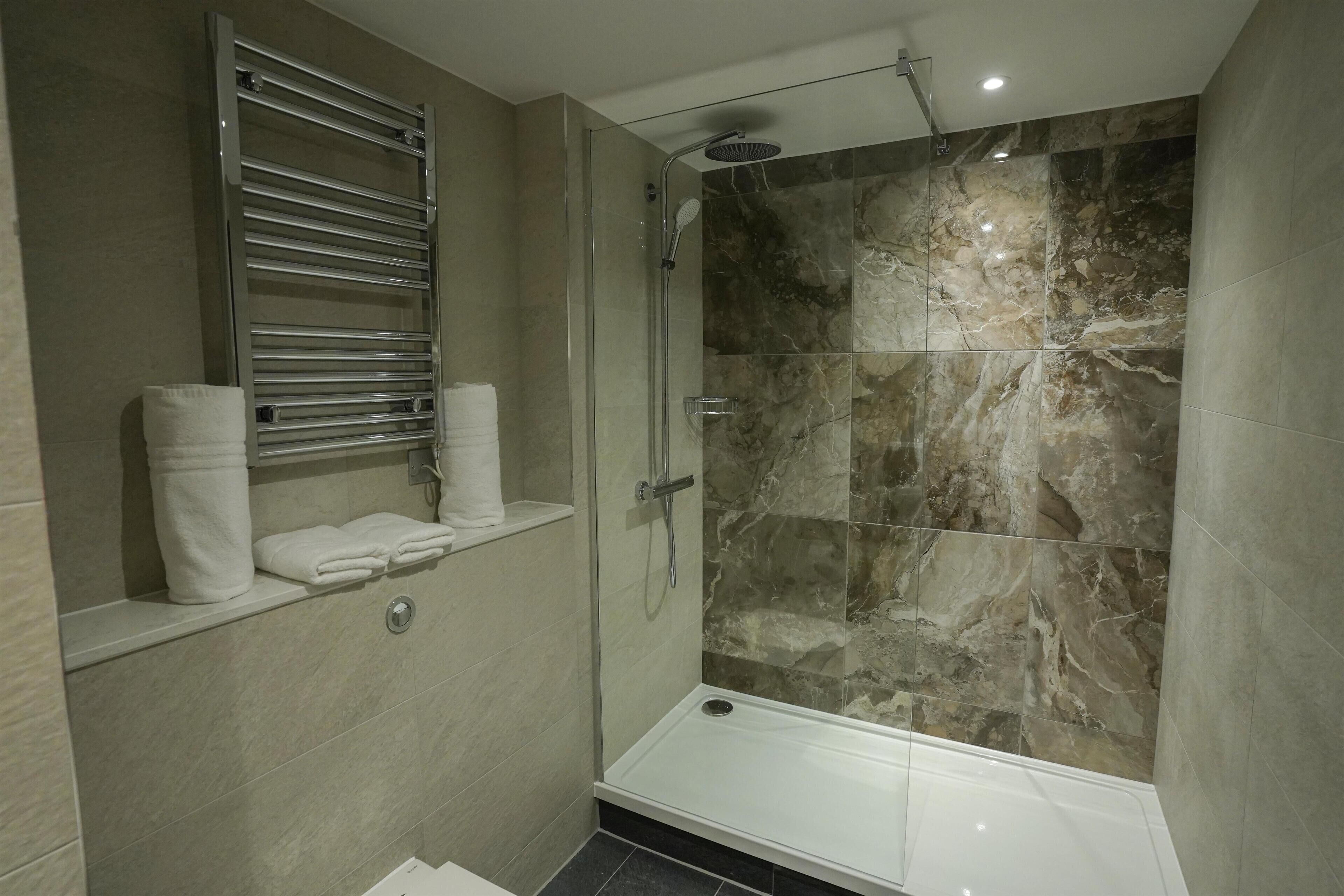 A modern bathroom with a glass-enclosed shower, marble tiles, and a built-in towel rack.