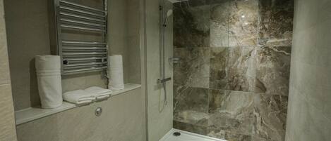 A modern bathroom with a glass-enclosed shower, marble tiles, and a built-in towel rack.