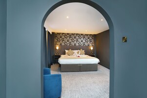 A modern hotel room with a large bed, dark walls, and a floral-patterned headboard.