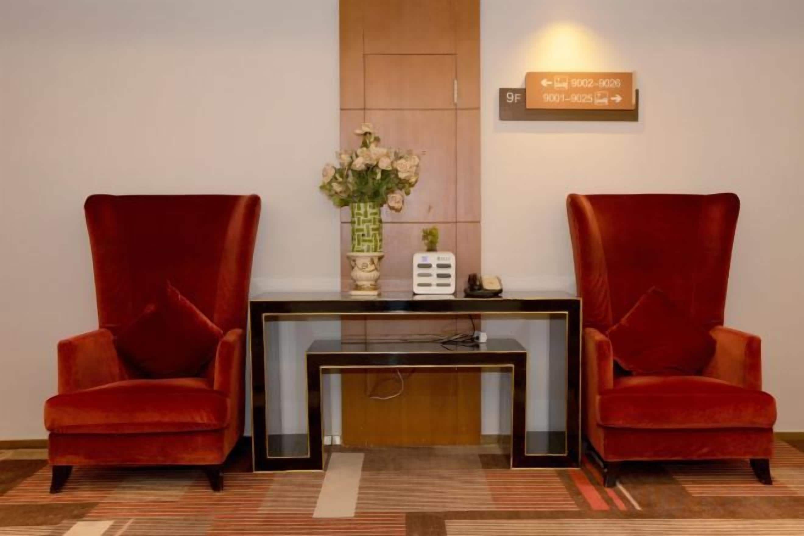 A reception area with two red chairs, a console table with a vase of flowers, and a sign above the door.