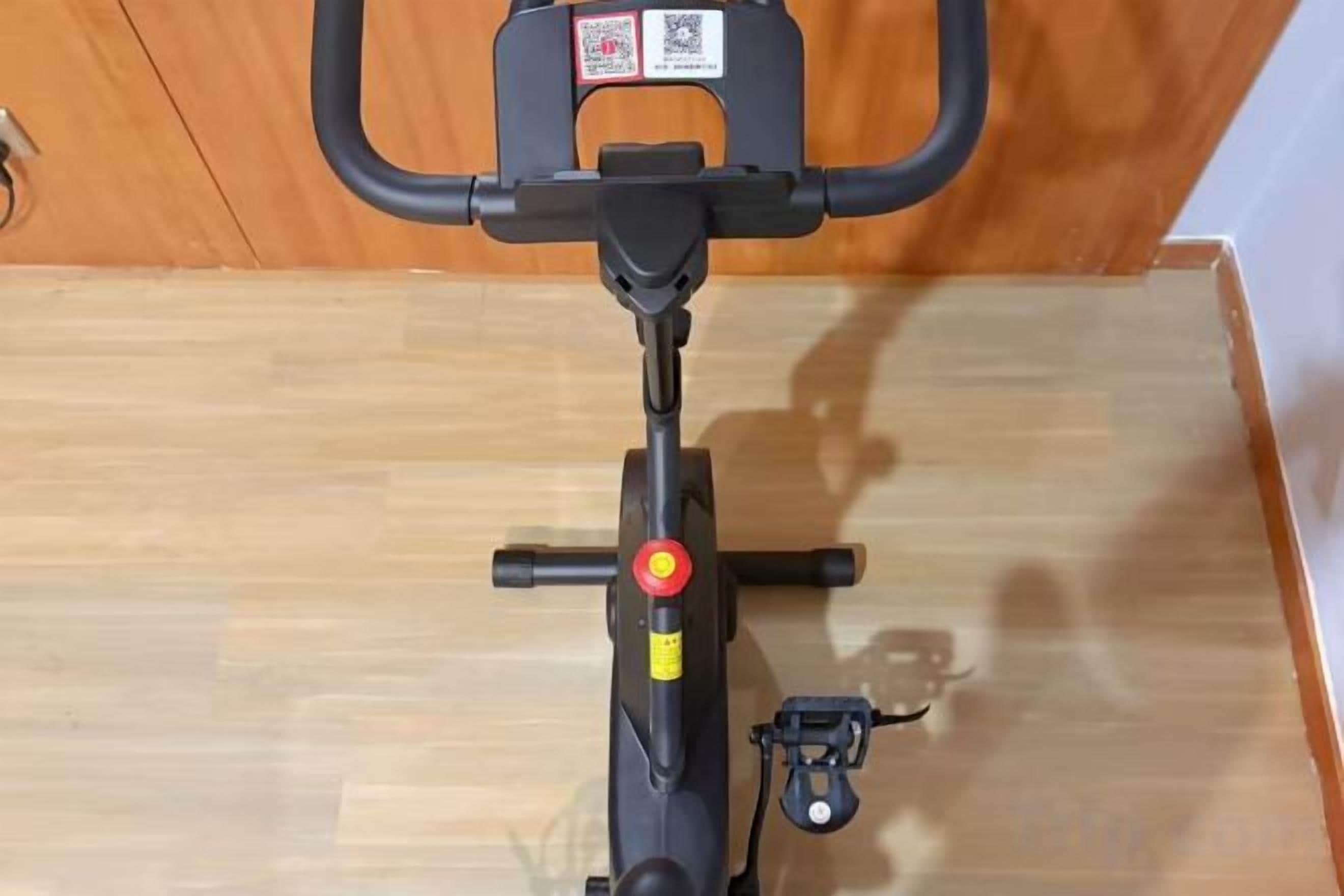 A stationary exercise bike with a QR code on the handlebar, a red button, and a small control knob.