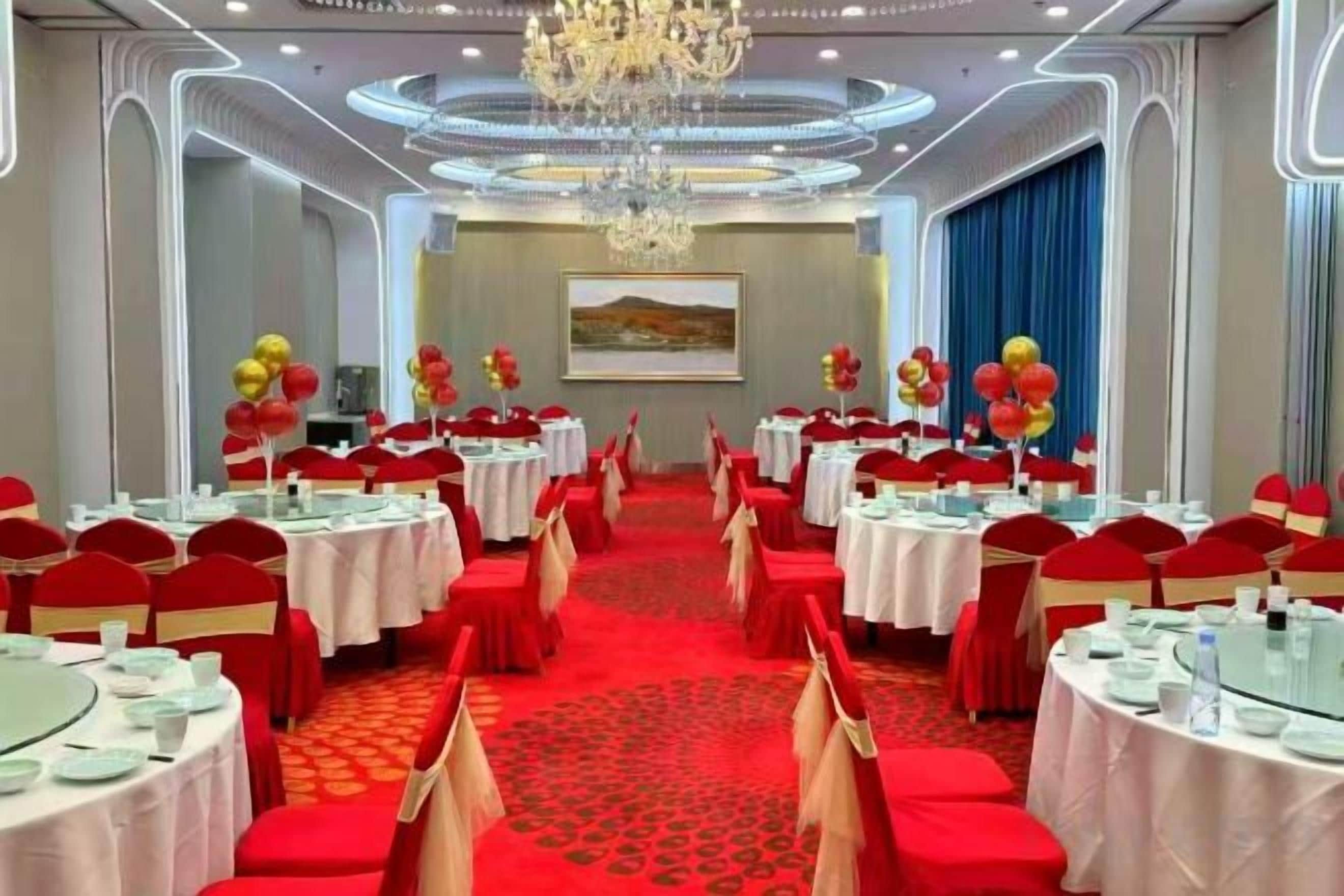 Een feestzaal met ronde tafels, rood-witte tafelkleden en rode stoelen.