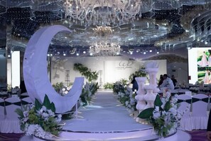 An indoor venue with a stage, floral decorations, and a chandelier. - Shuangman International Hotel (Ordos)