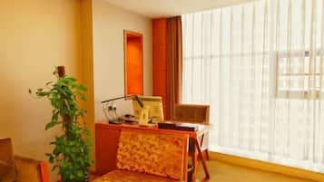 A room with a desk, chair, and a large window with sheer curtains.