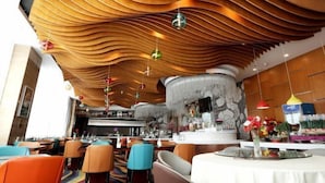 A restaurant with a unique wavy ceiling design, a bar area, and colorful seating. - Shuangman International Hotel (Ordos)