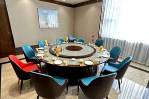 A conference room with a round table, blue and red chairs, and a painting on the wall. - Shuangman International Hotel (Ordos)