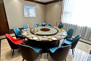 A conference room with a round table, blue and red chairs, and a painting on the wall.