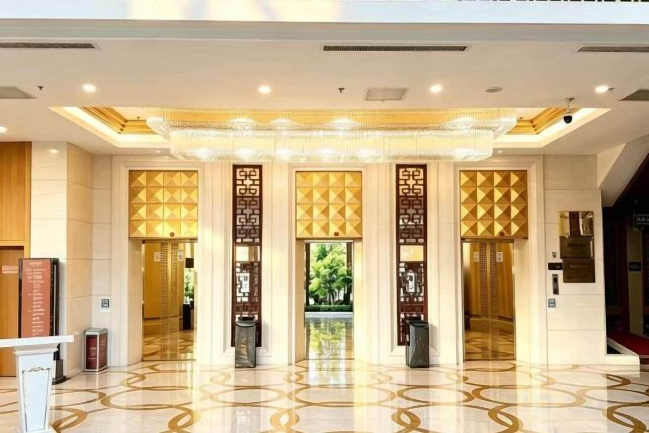 Un vestíbulo de hotel con diseño moderno, que cuenta con una lámpara central, piso pulido y paneles decorativos.