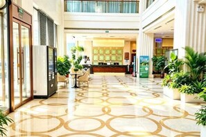 A hotel lobby with a patterned floor, reception desk, and potted plants. - Shuangman International Hotel (Ordos)