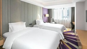 A hotel room with two beds, a desk, a chair, and a view of the city.