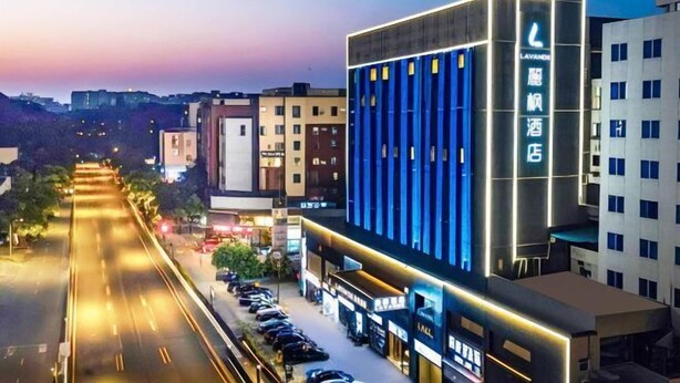 A modern hotel with a prominent vertical facade, a parking lot, and a street view.