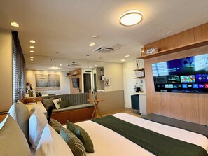 A hotel room with a bed, a sofa, a TV displaying a sports channel, and a small kitchenette. - Quarto de hotel Al Campinas Av Paulista (São Paulo)