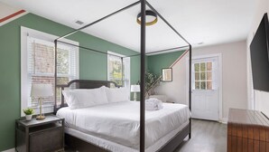 Een hemelbed met witte beddengoed, een nachtkastje met een lamp en een kleine plant.