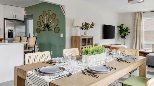 Een moderne eetruimte met een houten tafel voor vier personen, een groene accentmuur en een keuken op de achtergrond.