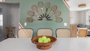 Een eetruimte met een tafel, stoelen en een wandmontage van tennisrackets.