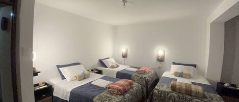 A hotel room with two beds, each with a pillow and a blanket. There are bedside tables with lamps and a ceiling fan.