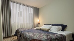 A hotel room with a bed, a nightstand, a lamp, a window with curtains, and a patterned rug. - Casa Marluc (Machu Picchu)