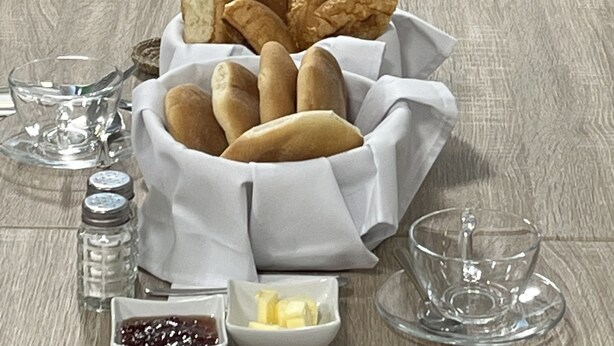 A dining table set with bread, butter, and condiments, surrounded by chairs and a view of greenery. - Casa Marluc (Machu Picchu)
