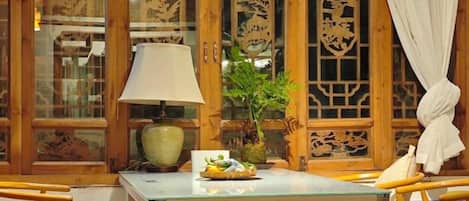 A room with a glass table, wooden furniture, a lamp, and a potted plant.