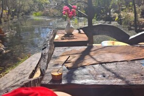 A wooden table with a vase of flowers, a glass of coffee, and a rustic setting by a body of water. - Xiangshangpin Hostel (Lijiang)